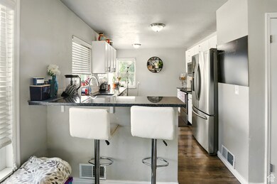 Kitchen featuring stainless steel appliances, white cabinets, dark wood-style floors, a peninsula, and a kitchen breakfast bar