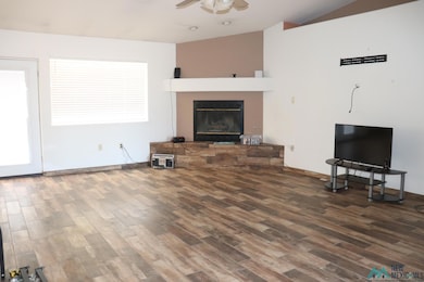 Unfurnished living room featuring a fireplace with raised hearth, dark wood finished floors, and a ceiling fan