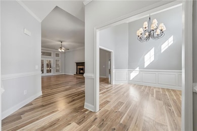 Foyer with a brick fireplace, ornamental molding, light wood-style flooring, a ceiling fan, and a wainscoted wall