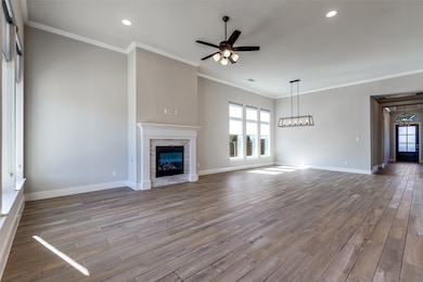 Unfurnished living room featuring healthy amount of natural light, crown molding, a ceiling fan, a stone fireplace, and wood finished floors