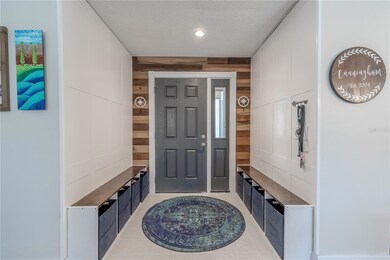 The  foyer blends crisp design with everyday practicality. Flanked by built-in benches on either side, each with deep cubbies for organized storage, this entryway is made for busy lives and smooth transitions. A rich, dark front door is framed by sidelights and set against a bold, rustic accent wall of horizontal wood planks that add warmth and texture. The paneled white walls bring a classic, tailored feel.