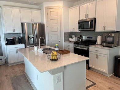 Kitchen with appliances with stainless steel finishes, tasteful backsplash, white cabinets, and light wood finished floors