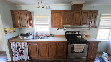 Kitchen with stainless steel electric range, light countertops, a textured ceiling, crown molding, and under cabinet range hood