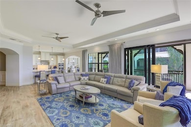 Living area featuring a raised ceiling, arched walkways, a ceiling fan, ornamental molding, and light wood-style floors