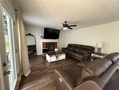 Living area featuring ceiling fan, dark wood-style floors, a brick fireplace, and a textured ceiling