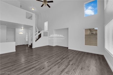 Unfurnished living room with a high ceiling, stairs, dark wood-type flooring, and a ceiling fan