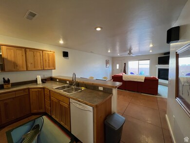 Kitchen with a peninsula, white dishwasher, a fireplace, dark tile patterned flooring, and dark countertops.  Some furnishings have changed.
