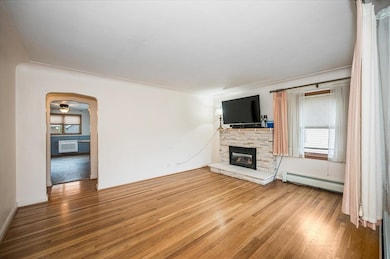 Unfurnished living room featuring a baseboard heating unit, wood finished floors, arched walkways, a fireplace, and ceiling fan