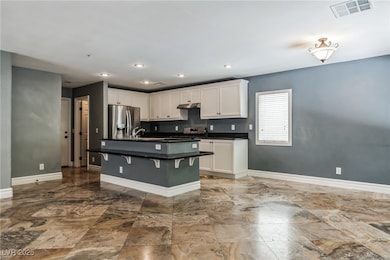 Kitchen with a center island with sink, stainless steel appliances, white cabinetry, a breakfast bar, and recessed lighting