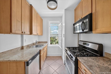 Kitchen featuring appliances with stainless steel finishes, light stone counters, and light tile patterned flooring