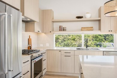 Kitchen with open shelves, appliances with stainless steel finishes, light brown cabinetry, and light stone countertops