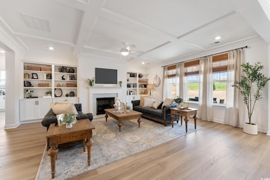 Living area featuring ceiling fan, coffered ceiling, light wood finished floors, a fireplace, and built in shelves