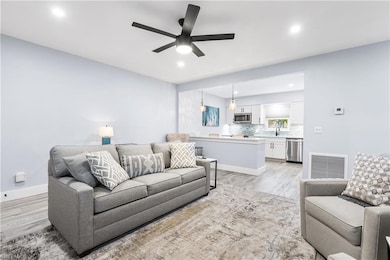 Living room featuring visible vents, baseboards, ceiling fan, and light wood finished floors
