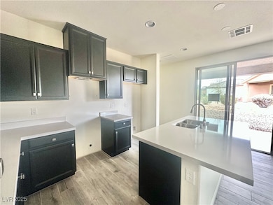 Kitchen with light wood finished floors, a center island with sink, dark cabinets, recessed lighting, and a kitchen bar