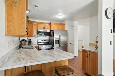 Kitchen featuring appliances with stainless steel finishes, a peninsula, light wood finished floors, a textured ceiling, and light countertops