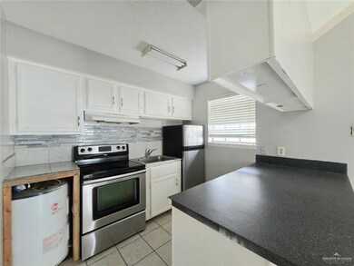 Kitchen featuring appliances with stainless steel finishes, under cabinet range hood, white cabinets, light tile patterned flooring, and dark countertops
