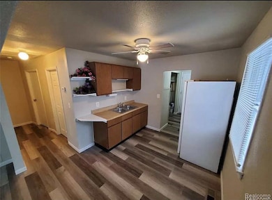 Kitchen featuring freestanding refrigerator, light countertops, brown cabinetry, open shelves, and dark wood-type flooring