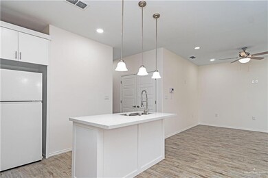 Kitchen featuring a center island with sink, white fridge, decorative light fixtures, and light wood-type flooring