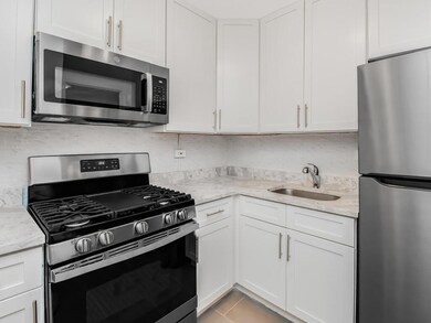 Kitchen featuring sink, stainless steel appliances, light tile patterned floors, light stone counters, and white cabinets