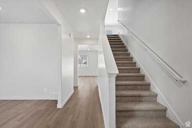 Staircase with wood finished floors, recessed lighting, and a textured ceiling