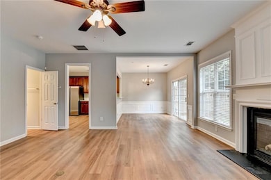 Unfurnished living room featuring ceiling fan, light wood-type flooring, a glass covered fireplace, a chandelier, and wainscoting