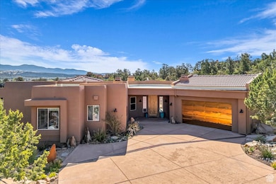 Pueblo-style house featuring a mountain view, a garage, a tile roof, stucco siding, and driveway