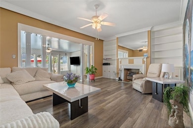 Living area with ceiling fan, crown molding, wood finished floors, and a fireplace with flush hearth