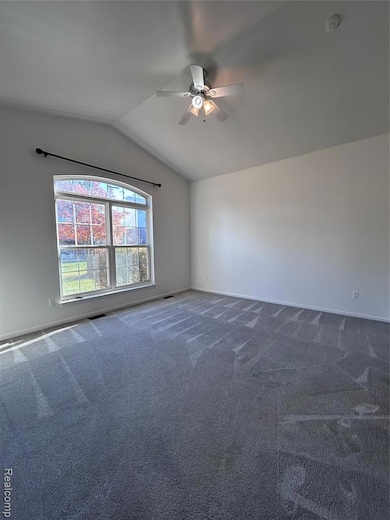 Carpeted empty room featuring vaulted ceiling and a ceiling fan