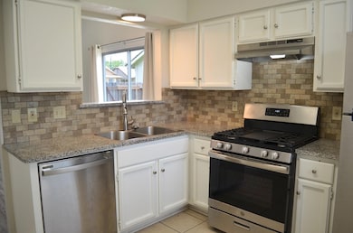 Kitchen featuring stainless steel appliances, white cabinetry, under cabinet range hood, and tasteful backsplash