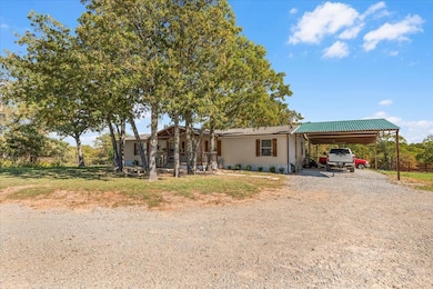 View of front of property featuring gravel driveway, an attached carport, a front yard, and a metal roof