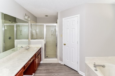 Full bathroom with a textured ceiling, vanity, light wood-style flooring, a stall shower, and a garden tub