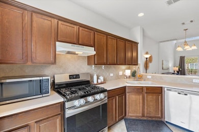 Kitchen featuring appliances with stainless steel finishes, brown cabinets, light countertops, tasteful backsplash, and under cabinet range hood