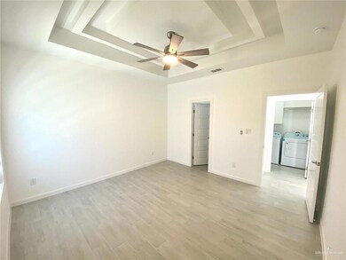 Unfurnished bedroom featuring a tray ceiling, washer and clothes dryer, light wood-type flooring, and a ceiling fan