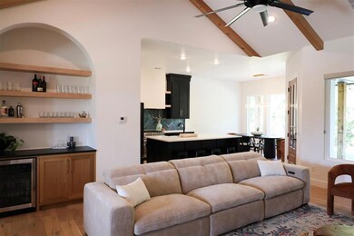 Living area featuring wine cooler, a bar, light wood-type flooring, beamed ceiling, and a ceiling fan