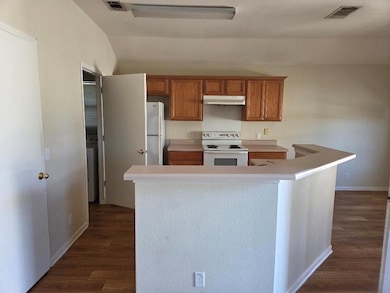 Kitchen with light countertops, white appliances, brown cabinetry, dark wood finished floors, and lofted ceiling