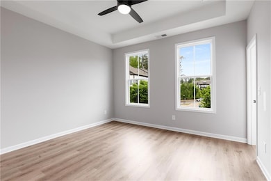 Empty room with light wood-type flooring, baseboards, a tray ceiling, and a ceiling fan