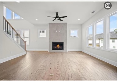 Unfurnished living room featuring light wood finished floors, healthy amount of natural light, a tile fireplace, ceiling fan, and recessed lighting