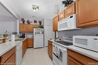 Kitchen featuring white appliances, light countertops, brown cabinetry, and light floors