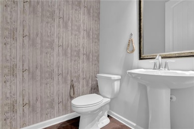 Half bath with baseboards, toilet, wood finished floors, and a sink