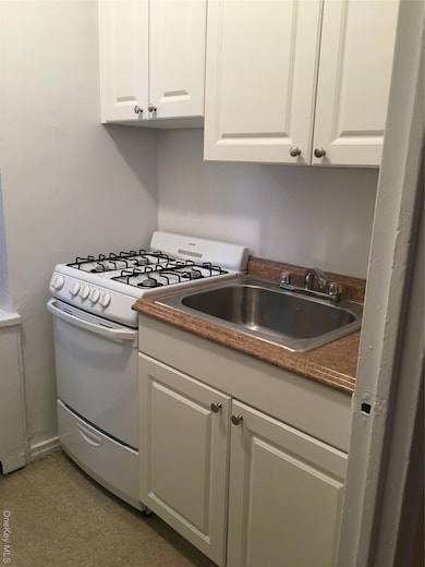 Kitchen with white gas range oven, white cabinetry, and dark countertops
