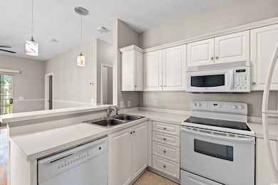 Kitchen with white appliances, a peninsula, white cabinetry, light countertops, and hanging light fixtures