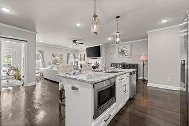 Kitchen featuring stainless steel appliances, a ceiling fan, open floor plan, a center island with sink, and light stone countertops