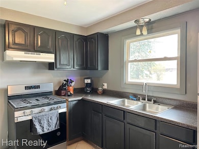 Kitchen with dark countertops, stainless steel gas range oven, under cabinet range hood, and light tile patterned flooring