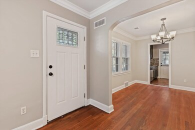Foyer entrance with crown molding, dark wood-style floors, arched walkways, and a chandelier