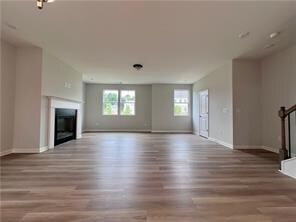 Unfurnished living room featuring wood finished floors and a glass covered fireplace