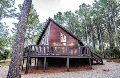 Back of house with a deck, log veneer siding, and view of wooded area