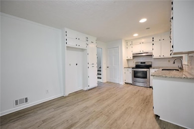 Kitchen with electric stove, a sink, under cabinet range hood, light wood-style floors, and white cabinets