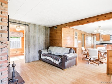 Living room with wood walls, light wood-type flooring, a chandelier, and beam ceiling