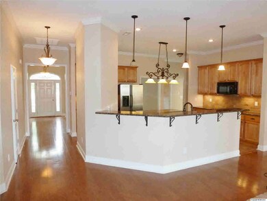 Kitchen has High Top Breakfast Bar with featuring Granite Counters, 3 Pendant Chandeliers, Hardwoods, and Foyer view of this open flowing floor plan.