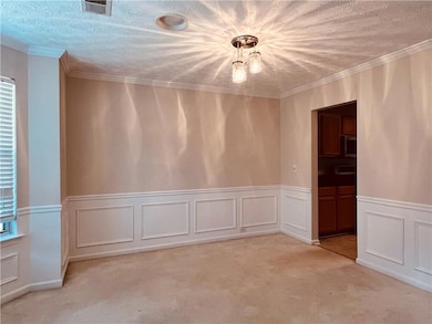 Unfurnished dining area featuring crown molding, a decorative wall, a textured ceiling, a wainscoted wall, and light carpet